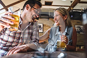 Happy friends having fun at bar - Young trendy couple drinking beer and laughing together