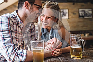 Happy friends having fun at bar - Young trendy couple drinking beer and laughing together