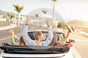 Happy friends having fun in convertible car at sunset in vacation - Young people making party and dancing in a cabrio auto