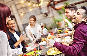 Happy friends having fun drinking red wine on balcony at private dinner party - Young people eating bbq food at fashion restaurant