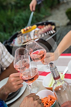 Happy friends having fun outdoors, hands toasting rose wine glass