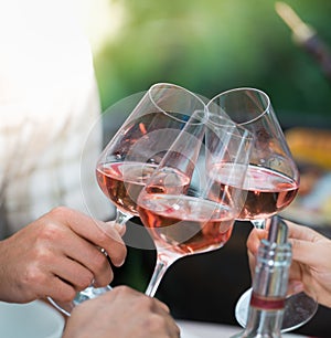 Happy friends having fun outdoors, hands toasting rose wine glass
