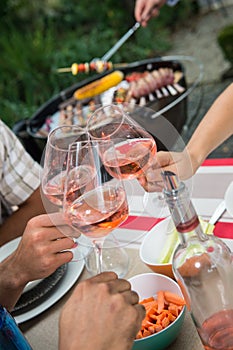 Happy friends having fun outdoors, hands toasting rose wine glass