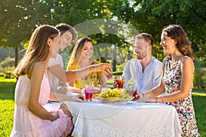 Happy friends having fun in park while they drink and eat around a picnic table in summer