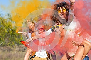 Happy friends having fun in the park with multicolored smoke bombs