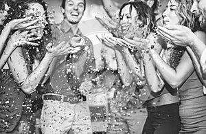 Happy friends having fun throwing confetti at vintage cocktail bar party - Young people hanging out on weekend holiday fest -