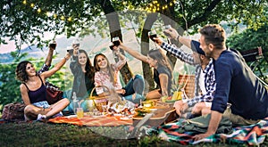 Happy friends having fun at vineyard on sunset - Young people millenial toasting at open air picnic under string light photo