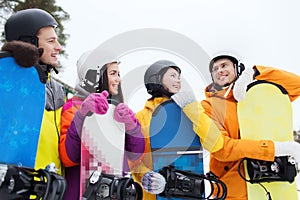 Happy friends in helmets with snowboards talking