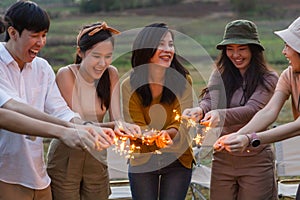 Happy friends holding fire sparkles. Group of young Travel join in fun at camping party in nature. Vacationers enjoy camping at