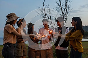 Happy friends holding fire sparkles. Group of young Travel join in fun at camping party in nature. Vacationers enjoy camping at