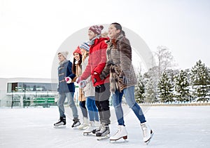 Happy friends ice skating on rink outdoors