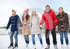 Happy friends ice skating on rink outdoors