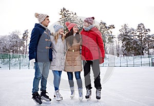 Happy friends ice skating on rink outdoors