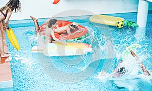 Happy friends jumping inside swimming pool  with tropical fruits lilos - Young people having fun diving into the water at beach