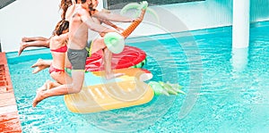 Happy friends jumping inside swimming pool with tropical lilos - Young people having fun diving into the water at beach resort