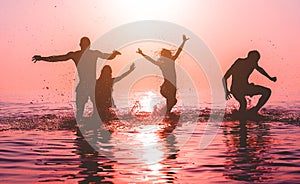 Happy friends jumping inside water on tropical beach at sunset - Group of young people having fun on summer vacation - Youth