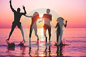 Happy friends jumping inside water on tropical beach at sunset - Group of young people having fun on summer vacation - Youth