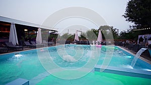 Happy friends jumping and splashing in swimming pool in luxury resort. Young men in swimwear having night party in