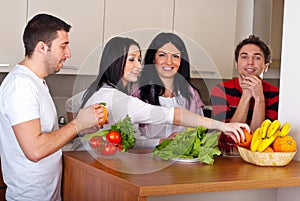 Happy friends in kitchen with vegetables