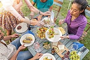 Happy friends laughing with big smile around the table in a summer diner. Woman serves the food at house patio. Smiles