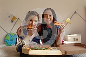 Happy friends lying on a bed and eating pizza.