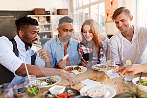 Happy friends with money paying bill at restaurant