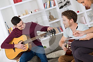 happy friends playing guitar and listening to music at home