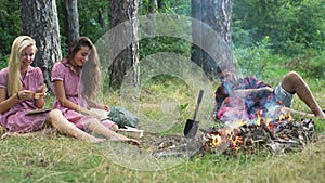 Happy friends playing music and enjoying bonfire in nature. Teenagers having fun at the forest. Friends sitting in the