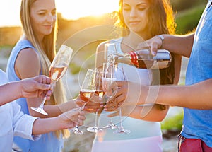 Happy friends pouring champagne sparkling wine into glasses outdoors at a beach