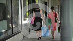 Happy friends with shopping paperbags walking in the city, beautiful women leaving mall after a successful shopping