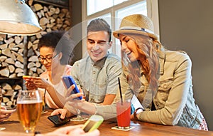 Happy friends with smartphones and drinks at bar