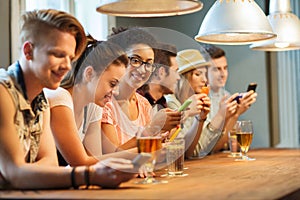 Happy friends with smartphones and drinks at bar