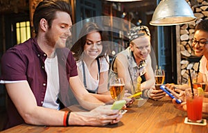 Happy friends with smartphones and drinks at bar
