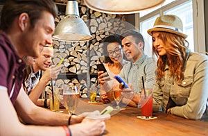 Happy friends with smartphones and drinks at bar