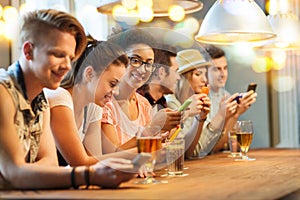 Happy friends with smartphones and drinks at bar