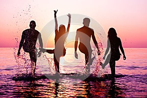 Happy friends splashing water on tropical beach at sunset - Group of young people having fun on summer vacation - Youth lifestyle