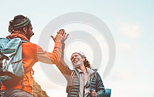 Happy friends stacking hands while doing trekking excursion on mountain - Young tourists walking and exploring the wild nature