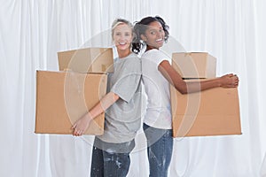 Happy friends standing back to back holding moving boxes