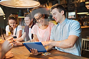 Happy friends with tablet pc and drinks at bar