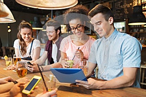 Happy friends with tablet pc and drinks at bar