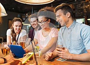 Happy friends with tablet pc and drinks at bar