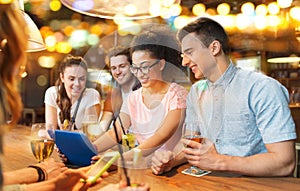 Happy friends with tablet pc and drinks at bar