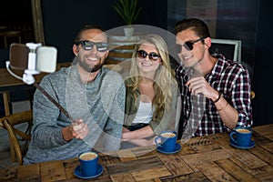 Happy friends taking selfie with monopod in coffee shop