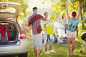 Happy friends unpacking car for camping trip