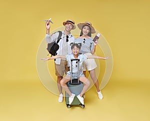 Happy fun asian family vacation portrait. Father, mother and daughters ready for travel flight with suitcase isolated on yellow