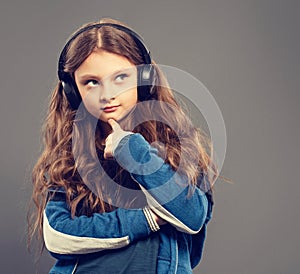 Happy fun kid girl listening the music in wireless earphones on grey background