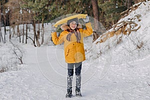 Happy fun kid holding a plastic sled on the background of snowy forest. Boy having fun on christmas holiday. Concept of winter