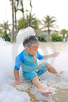 Happy and fun of little asian baby boy in swimming suit having fun in foam party at the pool outdoor