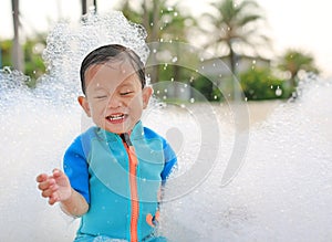 Happy and fun of little asian baby boy in swimming suit having fun in foam party at the pool outdoor