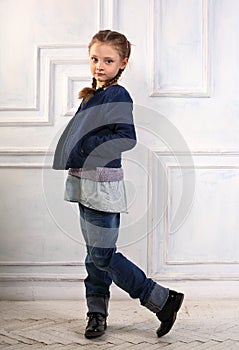 Happy fun smiling kid girl posing in fashion blue jeans, blouse, black boots and jacket on studio background. Full length